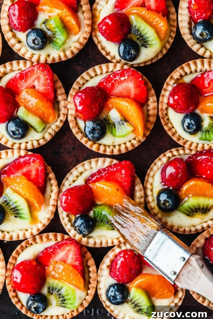 Fresh Fruit Tartlets with Silky Pastry Cream Recipe 16 A pastry brush brushing apricot jam on mini fruit tartlets.