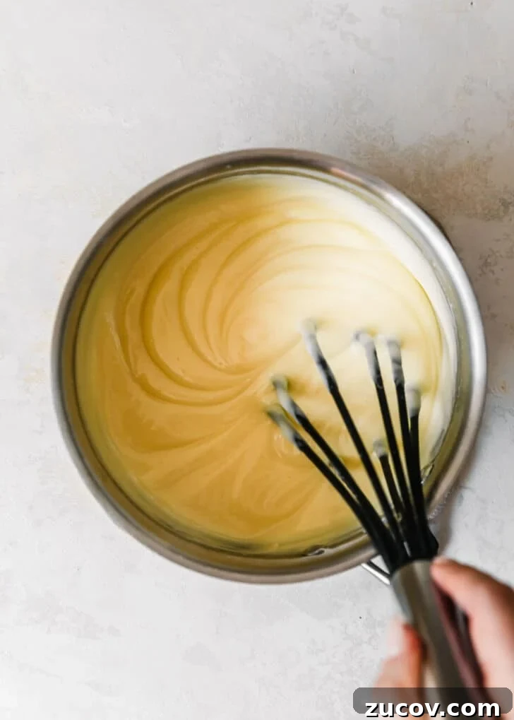 Fresh Fruit Tartlets with Silky Pastry Cream Recipe 9 A hand using a whisk to mix pastry cream in a silver pot