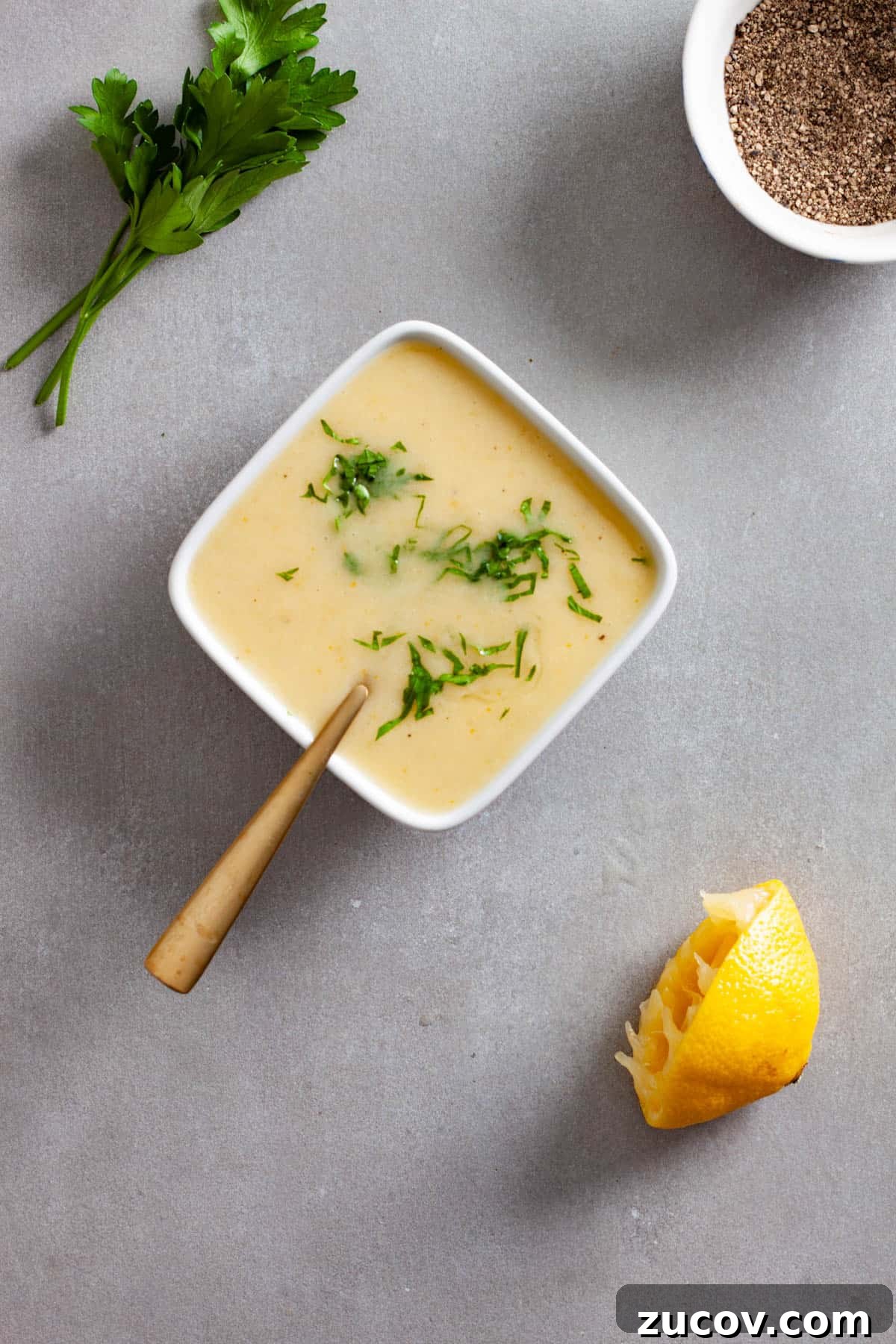 Preserved Lemon Vinaigrette Recipe for Bright, Tangy Salads 7 Chopped parsley and black pepper sprinkled on top of a preserved lemon vinaigrette in a small white bowl on a gray table.