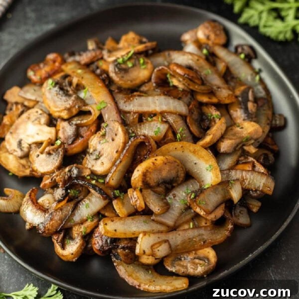 February Blackstone Chicken Recipes: What to Grill This Month 14 A black plate filled with Blackstone Sautéed Mushrooms and Onions for Steak, garnished with chopped herbs, sits on a dark surface.