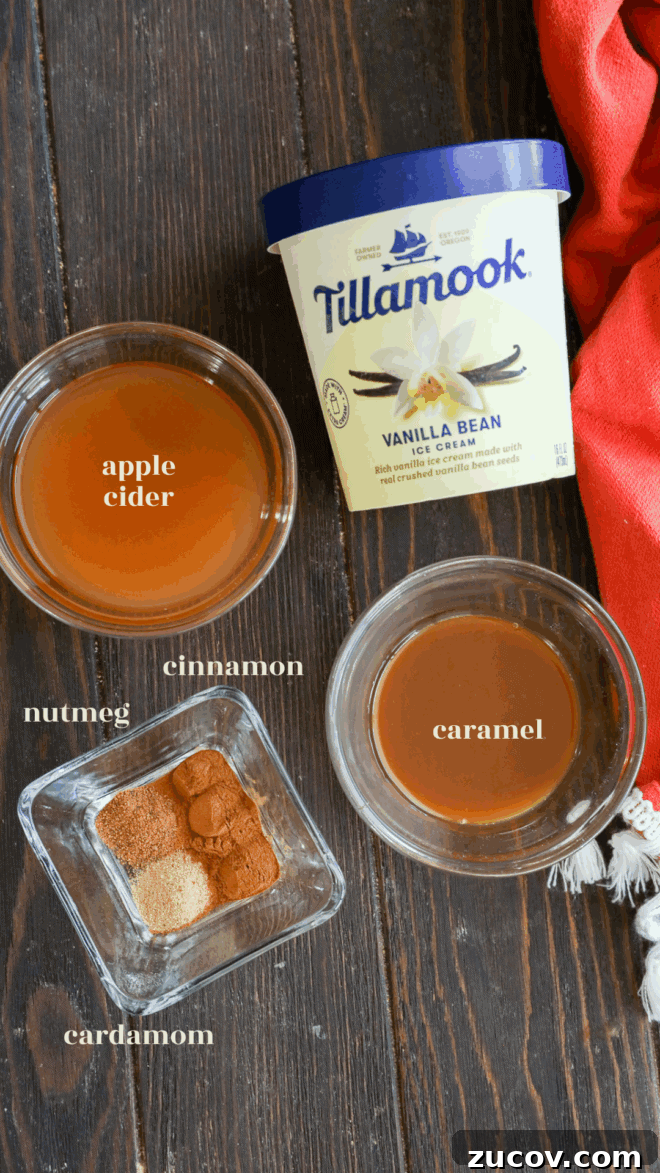 A tub of vanilla bean ice cream, glass bowls of apple cider and caramel, and spices arranged on a dark wooden surface.