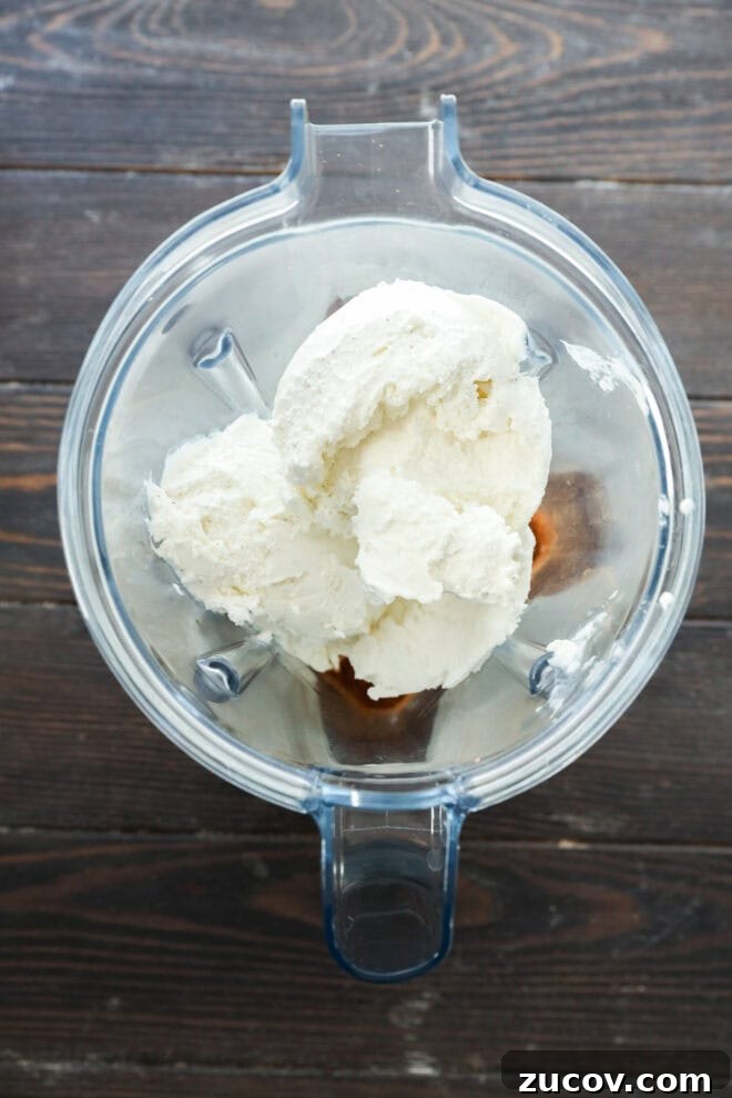 A top-down view of a blender containing scoops of vanilla ice cream and spices.