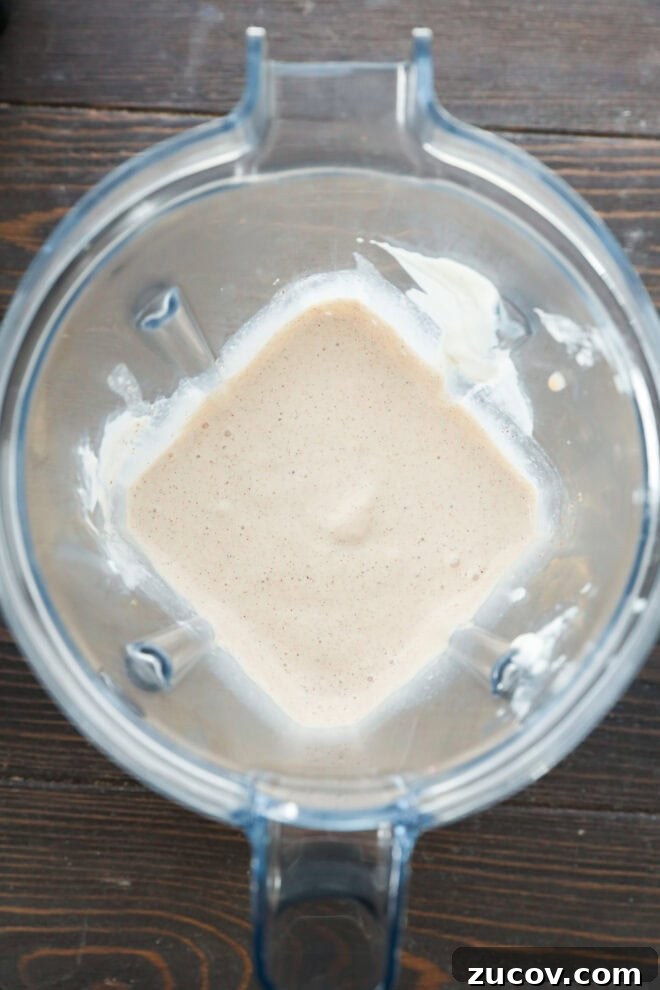 Overhead view of a blender containing a creamy, light beige mixture with some residue on the sides.