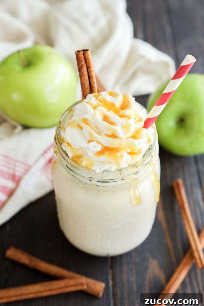 A mason jar filled with a creamy drink topped with whipped cream, caramel drizzle, and two cinnamon sticks, with a red and white striped straw.