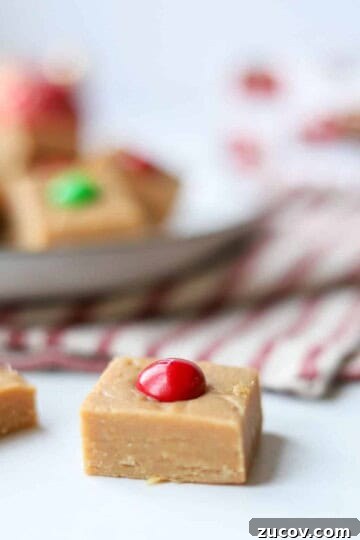 No bake peanut butter fudge topped with red m&m with plate of fudge in the background.