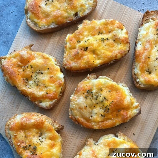 No-Knead Focaccia Recipe: Crispy, Olive Oil-Rich Bread in One Pan 18 Slices of bread topped with melted cheese and herbs make for delicious bites, beautifully arranged on a wooden cutting board placed on a gray surface.