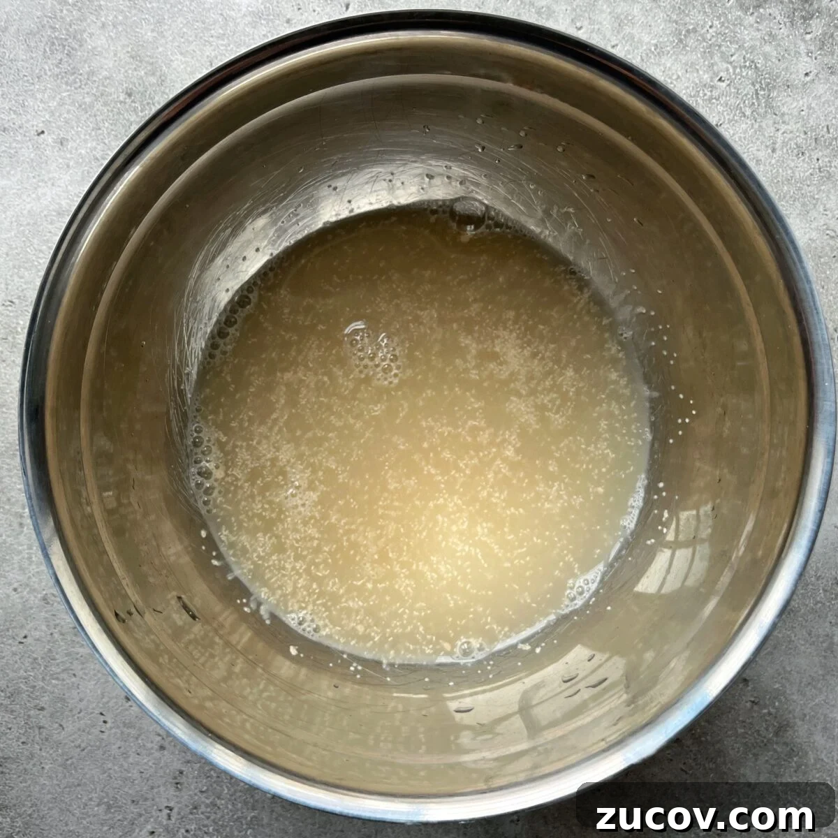 No-Knead Focaccia Recipe: Crispy, Olive Oil-Rich Bread in One Pan 8 A metal bowl containing water, honey, and active yeast.