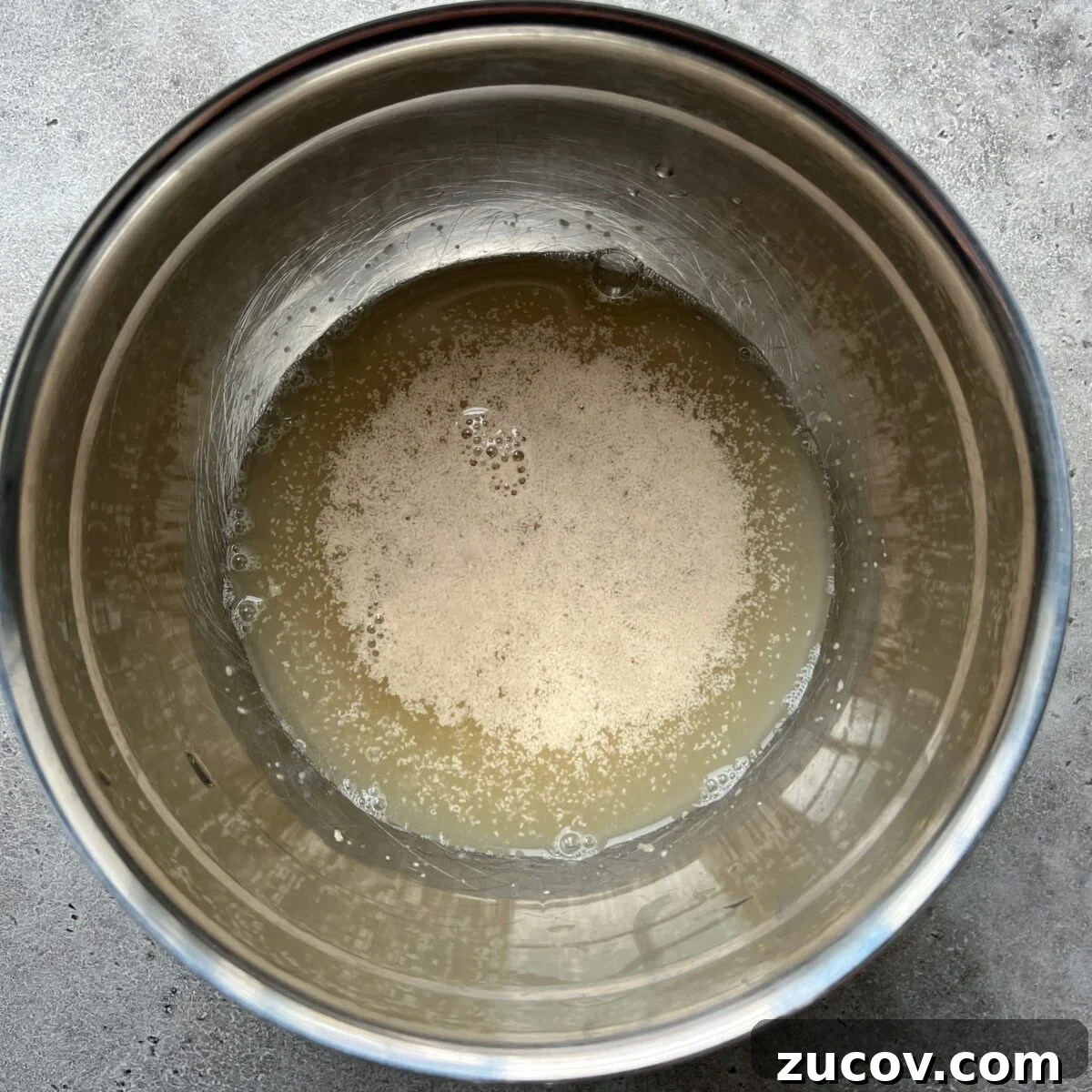 No-Knead Focaccia Recipe: Crispy, Olive Oil-Rich Bread in One Pan 9 A metal bowl containing water with yeast dissolving on the surface.