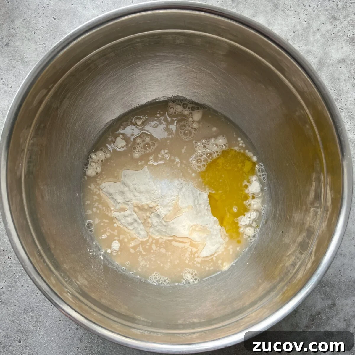 No-Knead Focaccia Recipe: Crispy, Olive Oil-Rich Bread in One Pan 10 A stainless steel mixing bowl containing flour, yeast, water, honey, and salt.