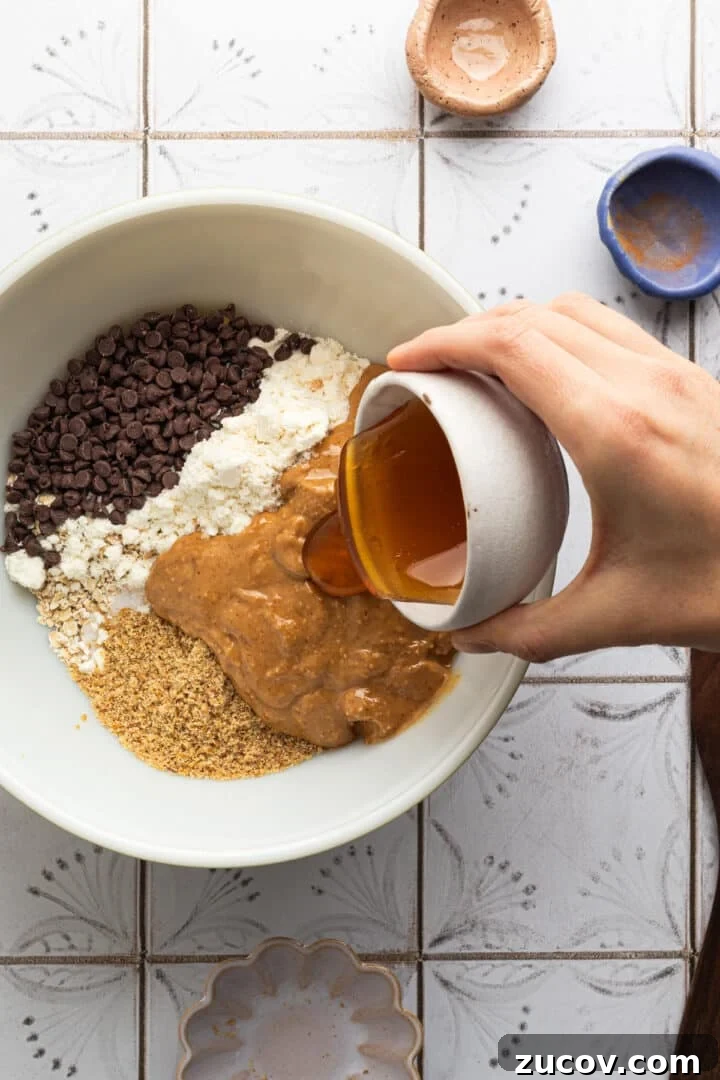 Cookie Dough Protein Balls: No-Bake Snack for Energy and Muscle 5 Ingredients for chocolate chip cookie dough protein balls being poured into a large white mixing bowl by a woman's hand