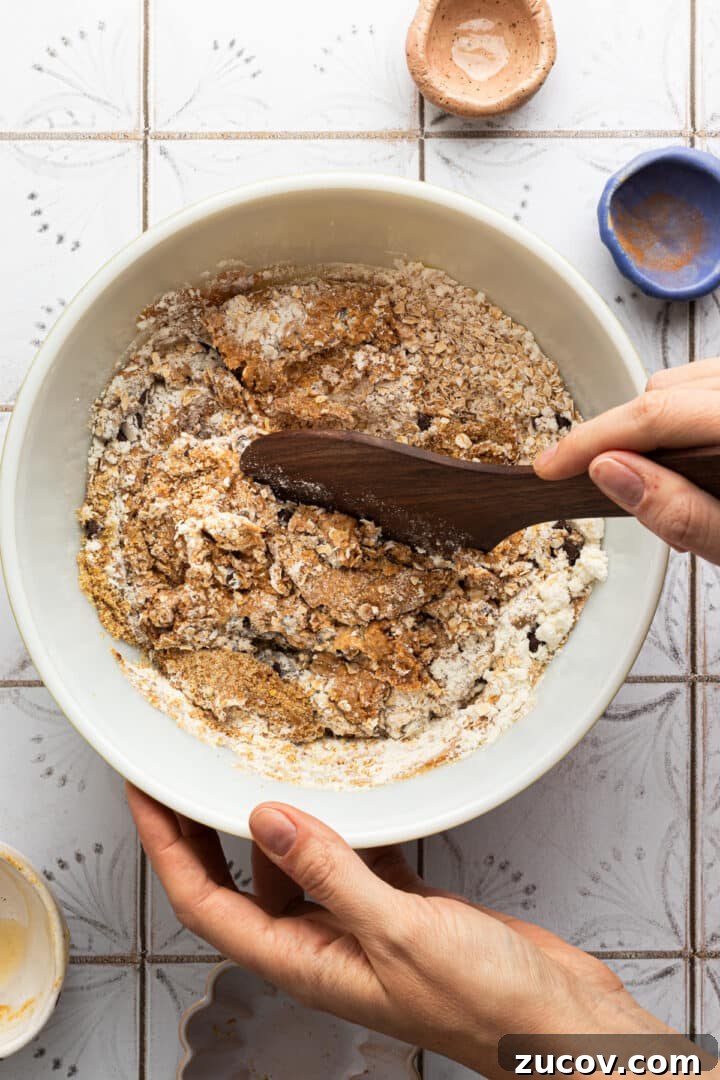 Cookie Dough Protein Balls: No-Bake Snack for Energy and Muscle 6 Cookie dough protein ball dough being mixed in a large, white mixing bowl with a wooden spoon