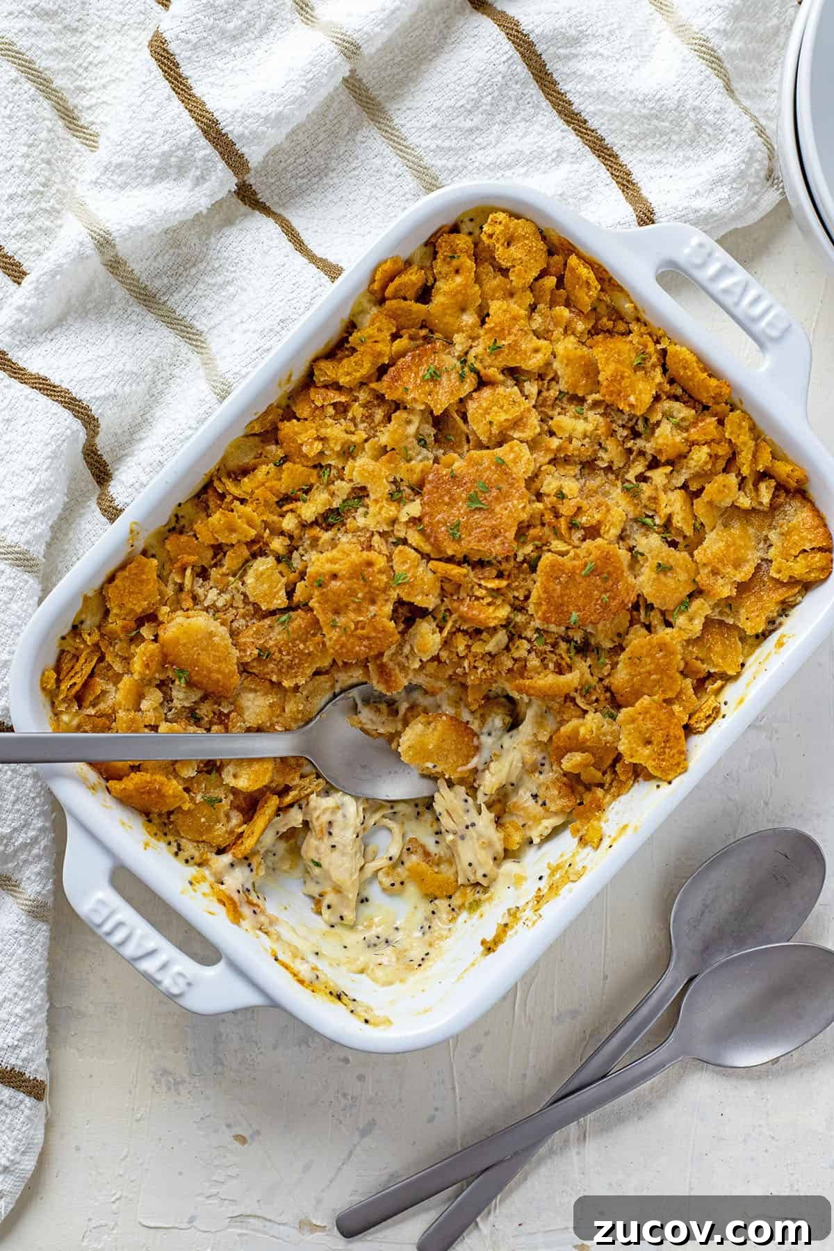 Southern Poppy Seed Chicken Casserole Recipe for Comforting Dinner 2 baked casserole in a white oblong dish with one serving removed and spoons on the side