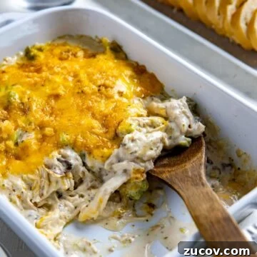 Baked casserole in white baking dish with wooden spoon removing a serving.