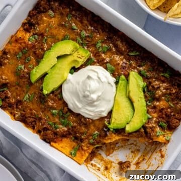 baked casserole in white rectangular dish. Topped with avocado slices and dollop of sour cream. One serving missing from casserole.