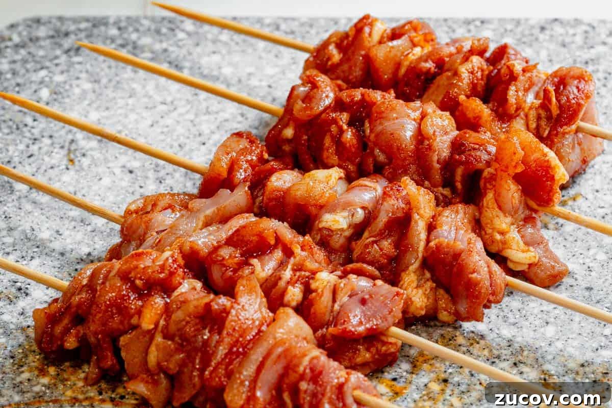 Bang Bang Chicken Skewers Recipe: Creamy Spicy Grilled Skewers 5 Seasoned and cubed chicken threaded on wooden skewers on a cutting board.