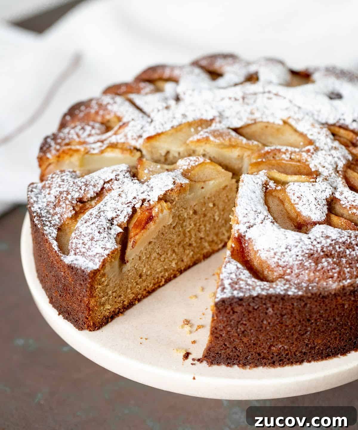 Moist Pear Cake Recipe with Cinnamon Glaze 2 Cut slice and rest of pear cake on pink cake stand on brown surface.
