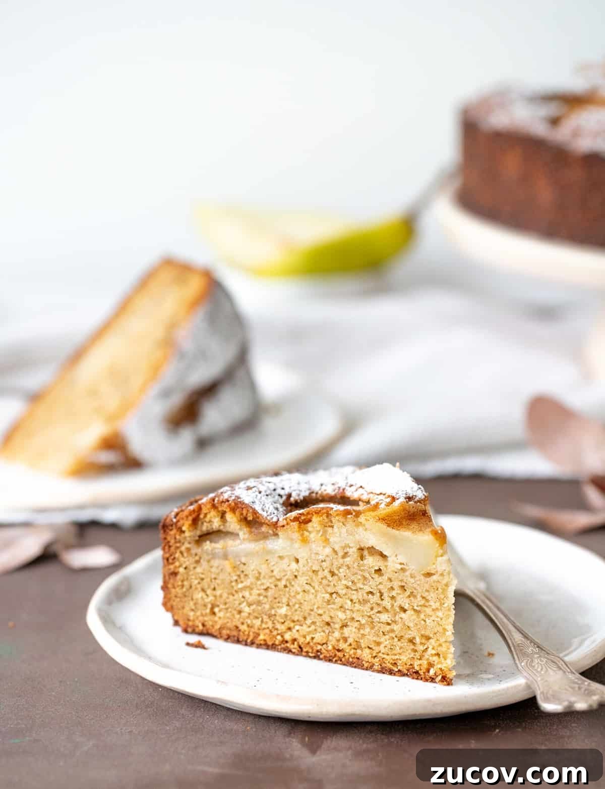 Pear sour cream coffee cake Slices of pear cake on white plates, brown surface, white background.
