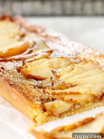 Close up of rectangular pear tart on a white surface with metal pan in the background.