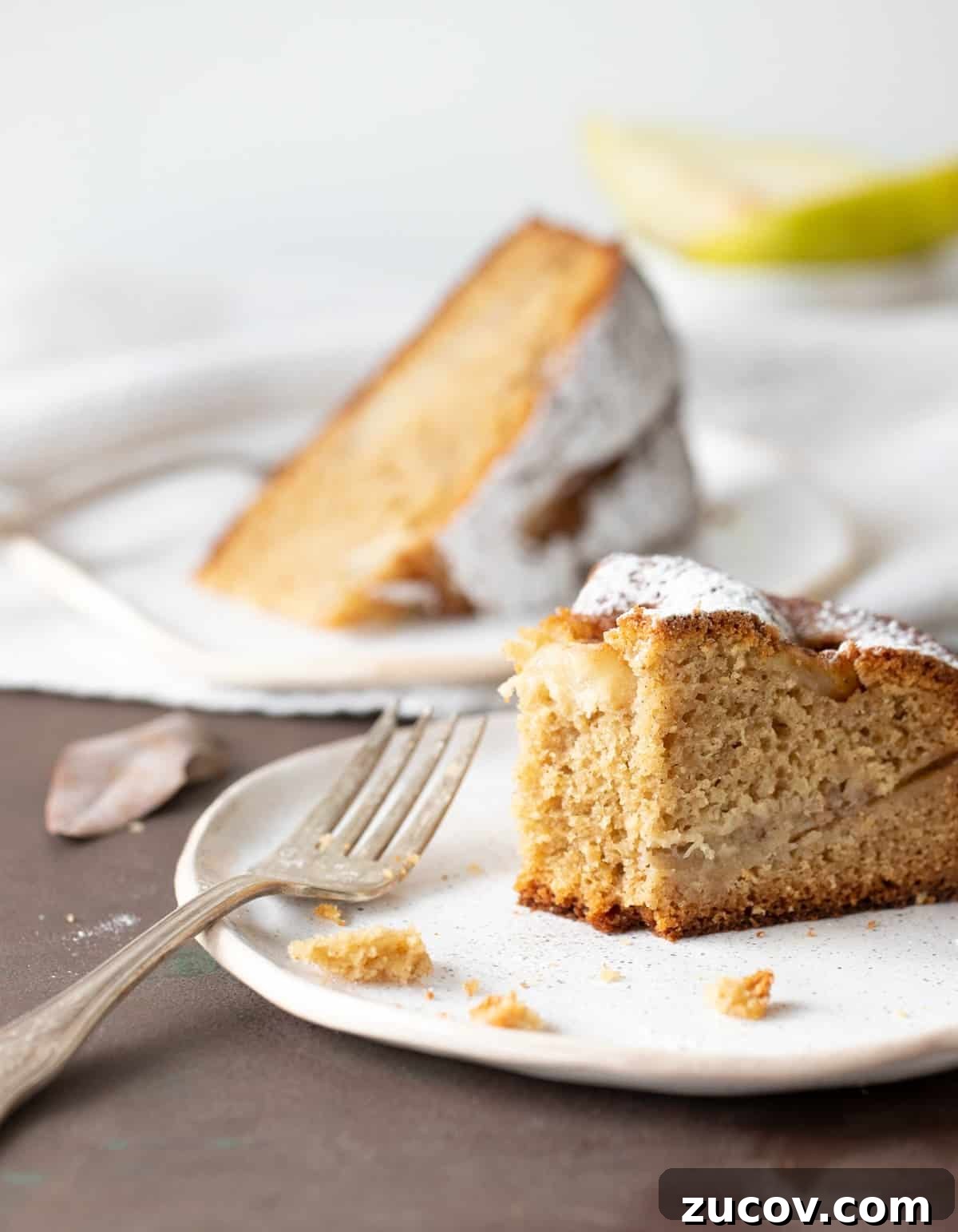 Moist Pear Cake Recipe with Cinnamon Glaze 3 Eaten slice of pear cake on white plate, silver fork, dark surface, whole slice in background