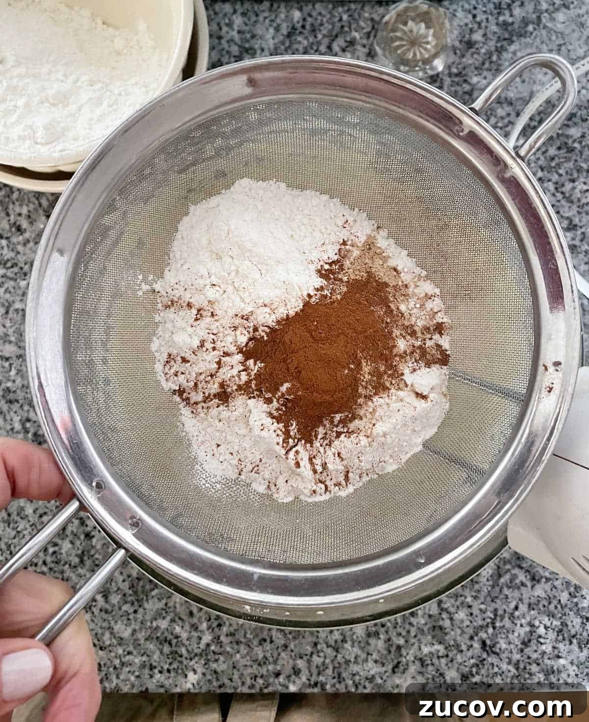 Moist Pear Cake Recipe with Cinnamon Glaze 6 Sifting flour and spices over bowl on a grey marble surface.