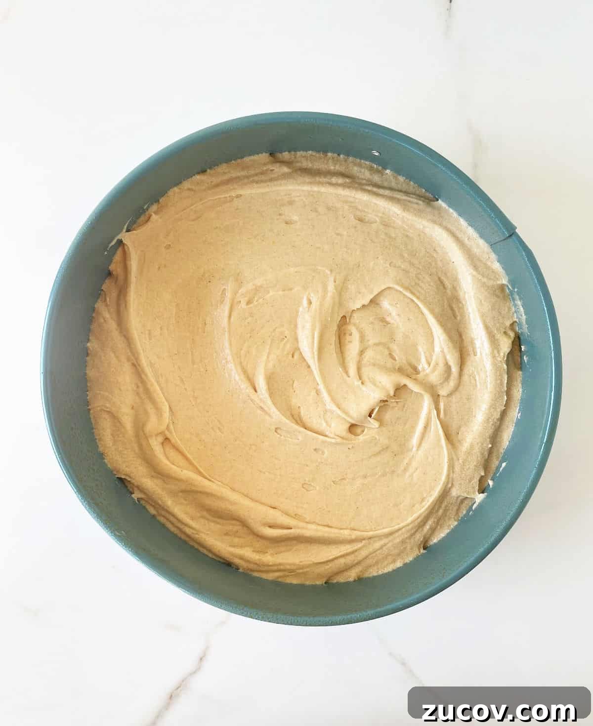 Moist Pear Cake Recipe with Cinnamon Glaze 7 Vanilla spice cake batter in a teal round cake pan on white marble.