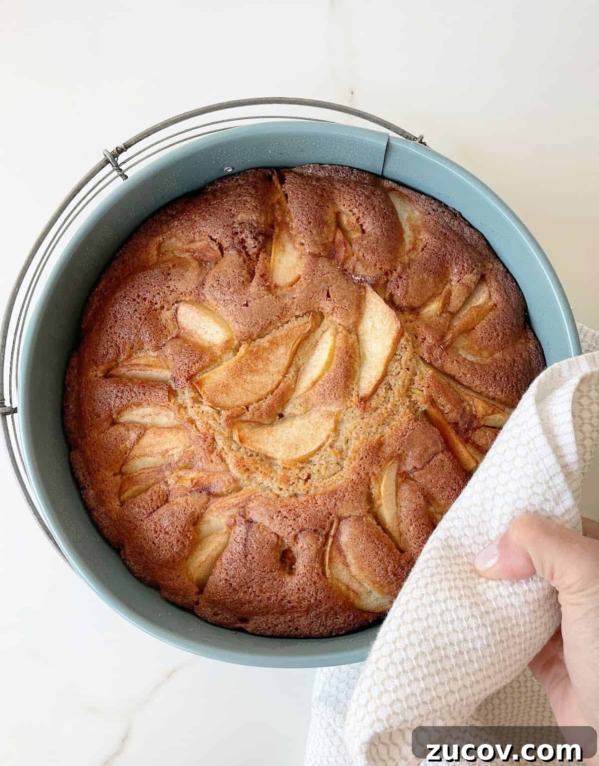 Moist Pear Cake Recipe with Cinnamon Glaze 9 Hand with towel placing baked pear cake on wire rack, white marble surface