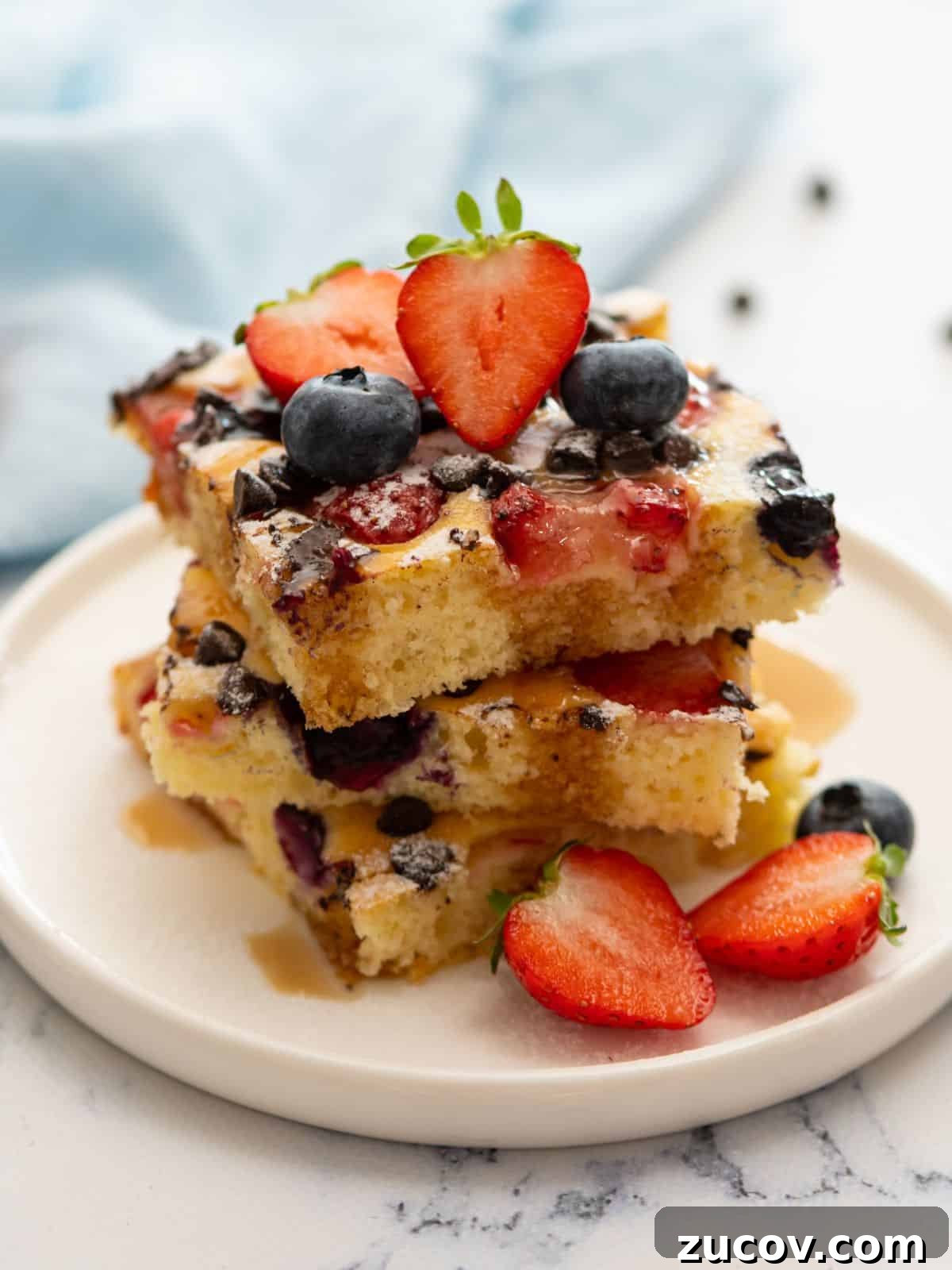 Sheet Pan Pancake Recipe Squares of sheet pan pancakes on white plate topped with maple syrup and powdered sugar with fresh berries to the side.