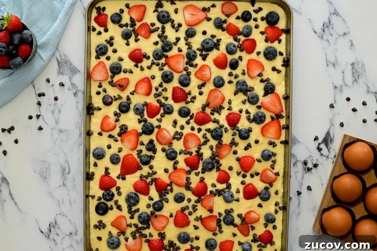 Pancakes for a Crowd Pancake batter spread out on half-sheet pan topped with berries and mini chocolate chips.