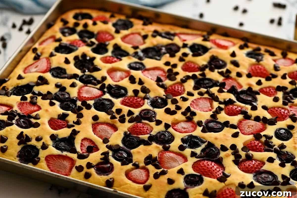 Sheet Pan Pancake Baked pancake on sheet pan topped with berries and chocolate chips.