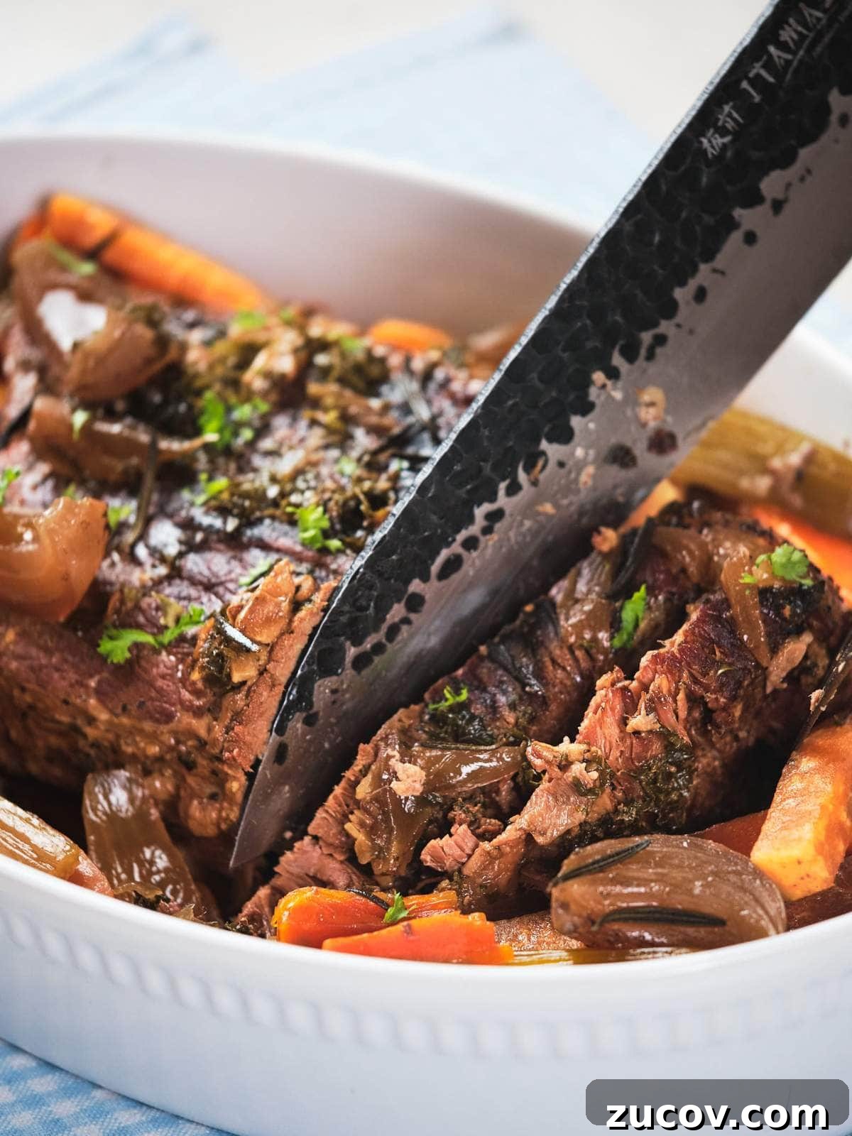 28 Low-Histamine Recipes for Histamine Intolerance-Friendly Meals 23 A close-up of keto pot roast with carrots and onions in a white serving dish, garnished with herbs, with a knife resting on top.