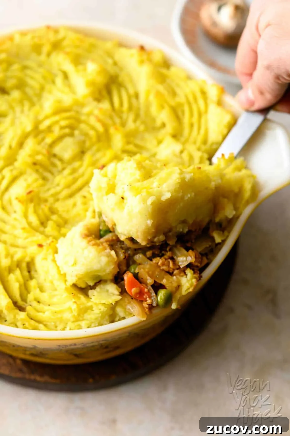 Savory Vegan Shepherd’s Pie with a Flavorful Twist 7 One casserole dish filled with a vegan shepherd's pie, being scooped out with a steel serving spoon, on a light linoleum background.