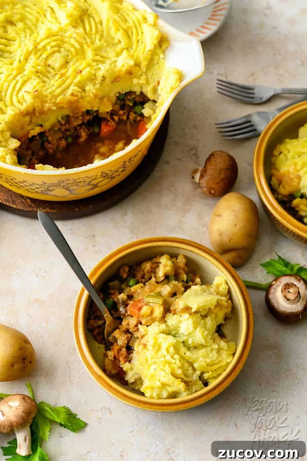 Savory Vegan Shepherd’s Pie with a Flavorful Twist 11 One casserole dish filled with a vegan shepherd's pie, spooned into two bowls, with potatoes and mushrooms scattered around them, on a light linoleum background.