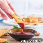 Crispy Roasted Parmesan Potato Wedges with Garlic and Herbs 10 Hand dipping a roasted potato into ketchup.