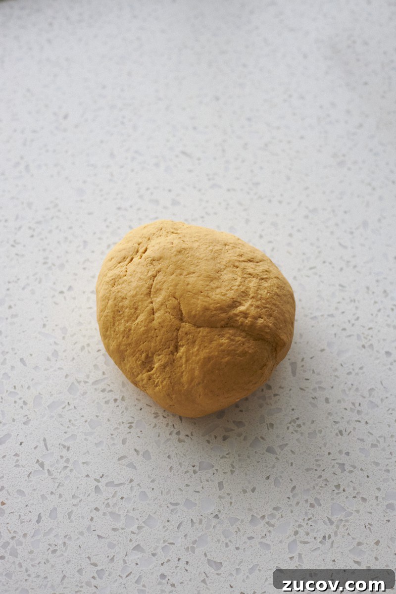 Sourdough-Discard Pumpkin Dinner Rolls for Fall Baking 6 Kneaded dough on a work surface.