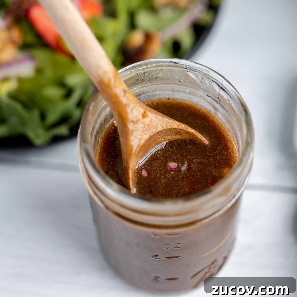 Crisp Apple and Walnut Salad with Maple Dijon Dressing 4 A jar of balsamic dressing with a wooden spoon. Salad in the background.