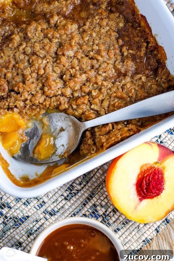 Peach Oat Crumble Recipe: Rustic Summer Dessert with Fresh Peaches 4 top view of peach crumble with an oat topping in a white casserole dish with a spoon