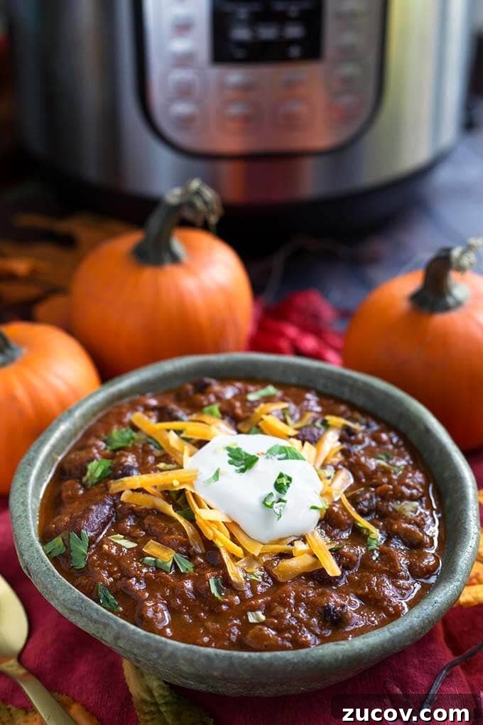 Instant Pot Pumpkin Chili Recipe for Cozy Weeknight Dinners 4 Pumpkin Chili topped with shredded cheese and sour cream in a turquoise bowl in front of a pressure cooker