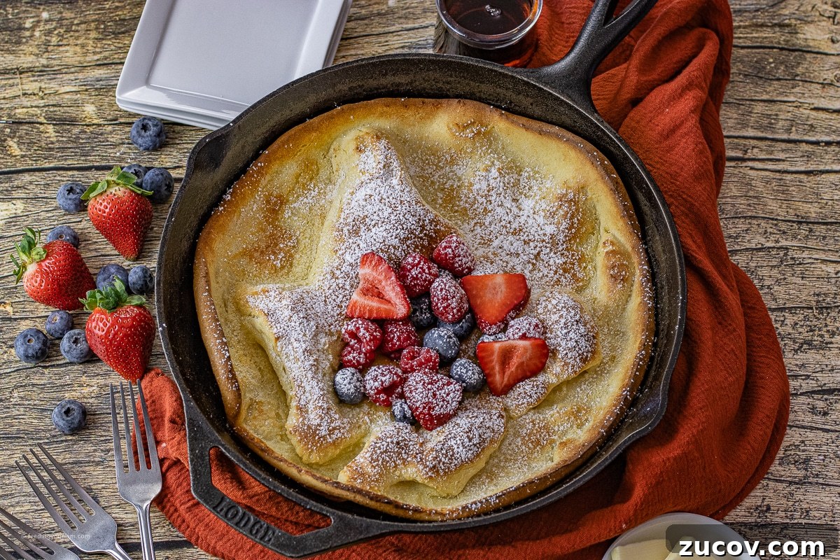 Cast-Iron Dutch Baby Pancake Recipe for a Crispy, Fluffy Oven Skillet 5 cast iron skillet with a dutch baby pancake baked inside with fruit and powdered sugar on top of it
