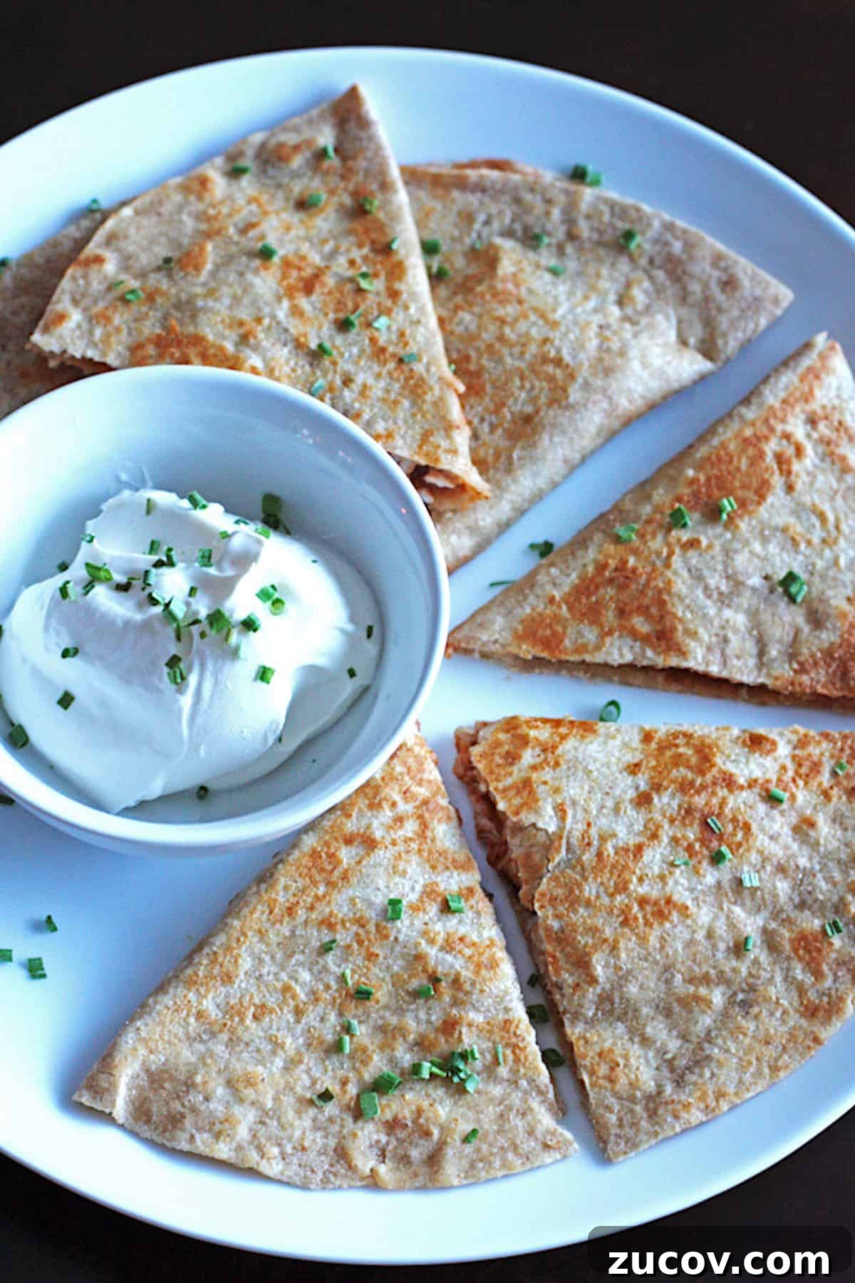 Smoky BBQ Chicken Quesadillas with Melty Cheese and Cilantro 2 Sliced barbecue chicken quesadillas on a white plate with a small bowl of sour cream.