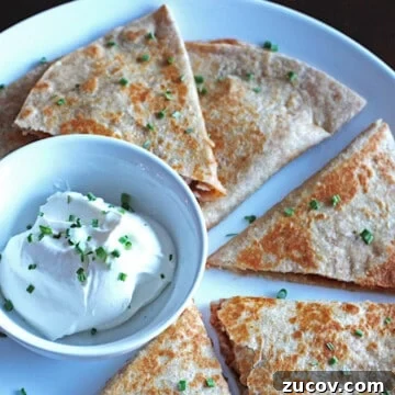 Smoky BBQ Chicken Quesadillas with Melty Cheese and Cilantro 9 Sliced barbecue chicken quesadillas on a white plate with a small bowl of sour cream.