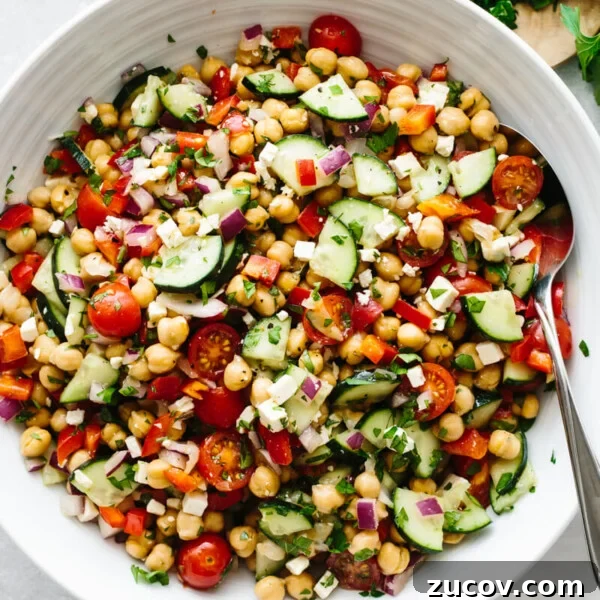 A large white bowl of Mediterranean chickpea salad on a table with parsley leaves.