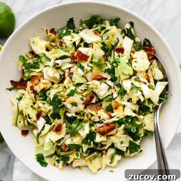 A bowl of cilantro lime bacon coleslaw next to limes.