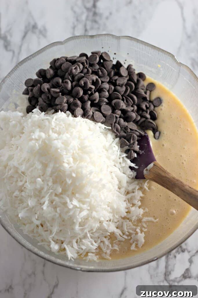Coconut Butter Bars Recipe with Creamy Coconut Filling 8 Chocolate chips being added to batter in a glass bowl.