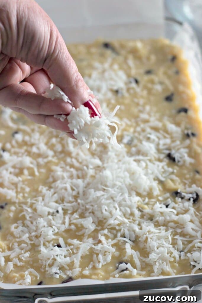 Coconut Butter Bars Recipe with Creamy Coconut Filling 9 Coconut being sprinkled on top of batter in a baking dish.