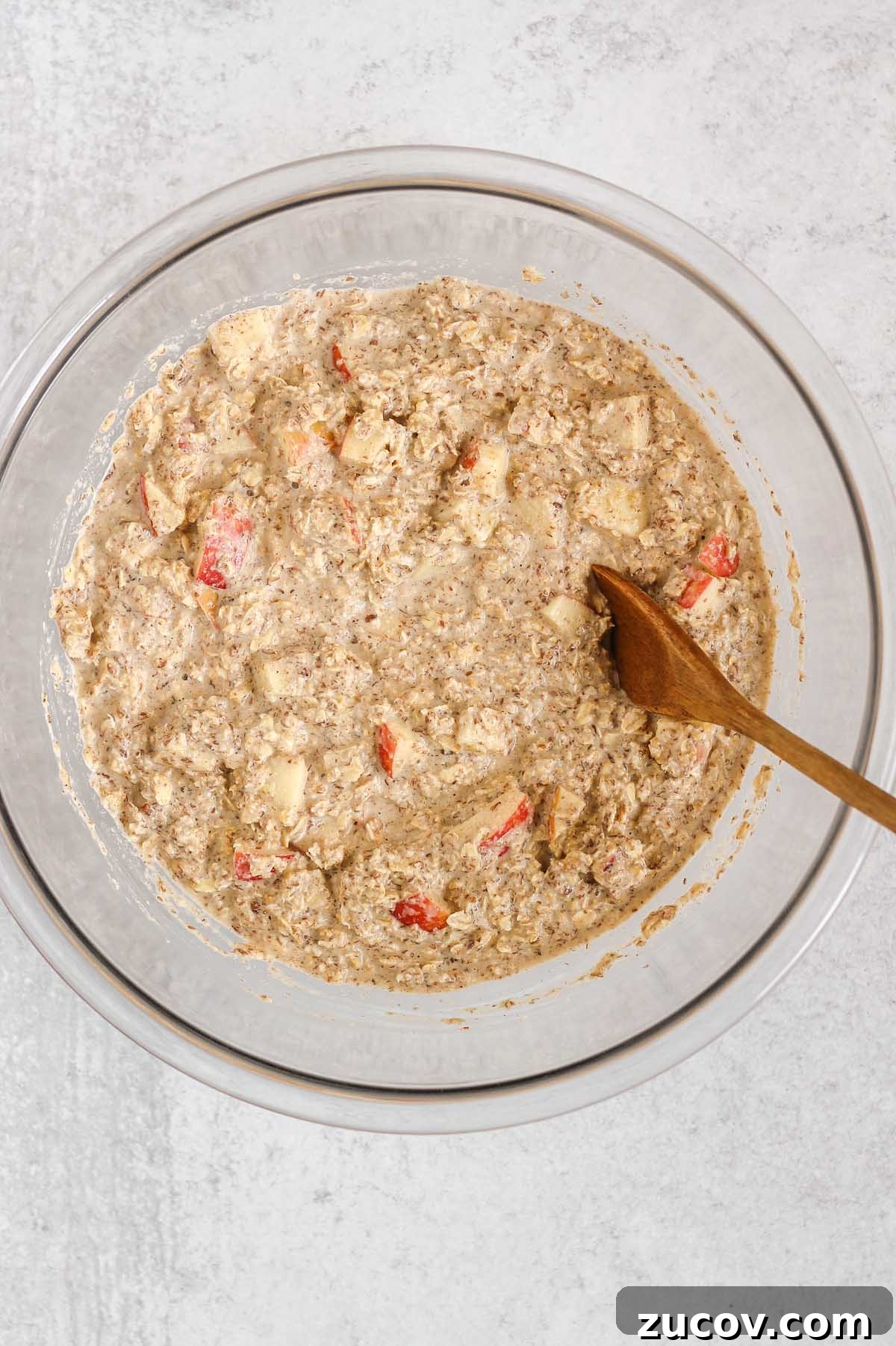 Oatmeal mix with apples in a large glass mixing bowl.