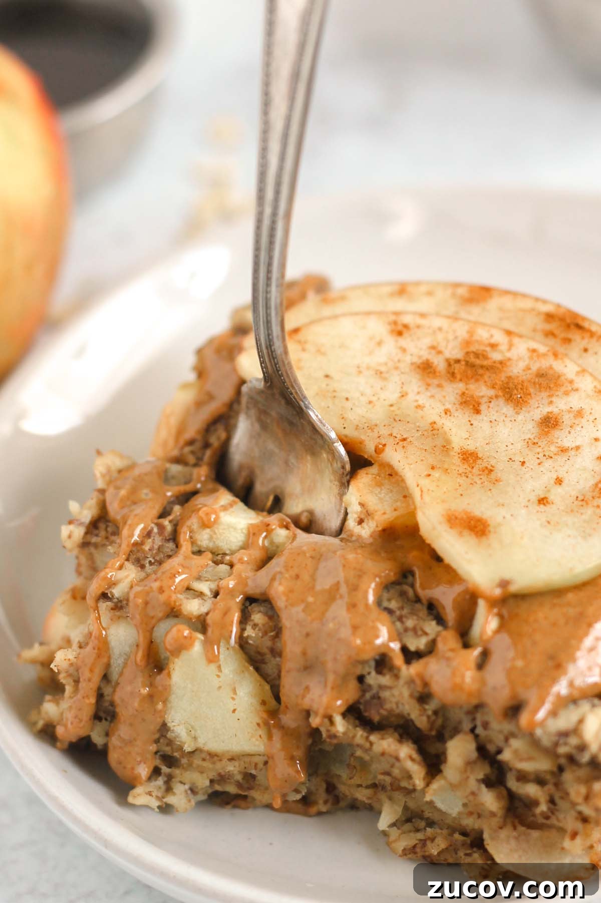 Fork taking a bite out of a square piece of apple baked oatmeal topped with sliced apples and almond butter.