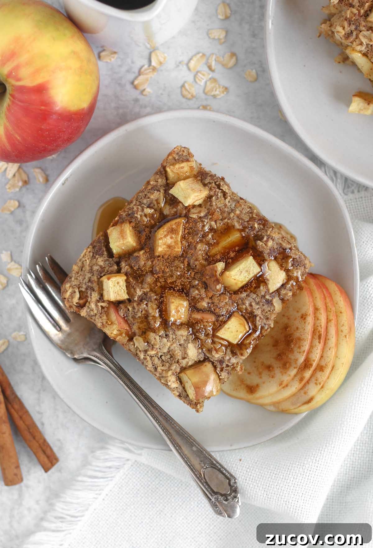 Square piece of apple cinnamon baked oatmeal topped maple syrup on a round plate with a vintage fork.