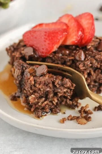Gold fork cutting a bite off of a piece of chocolate baked oats topped with strawberries.
