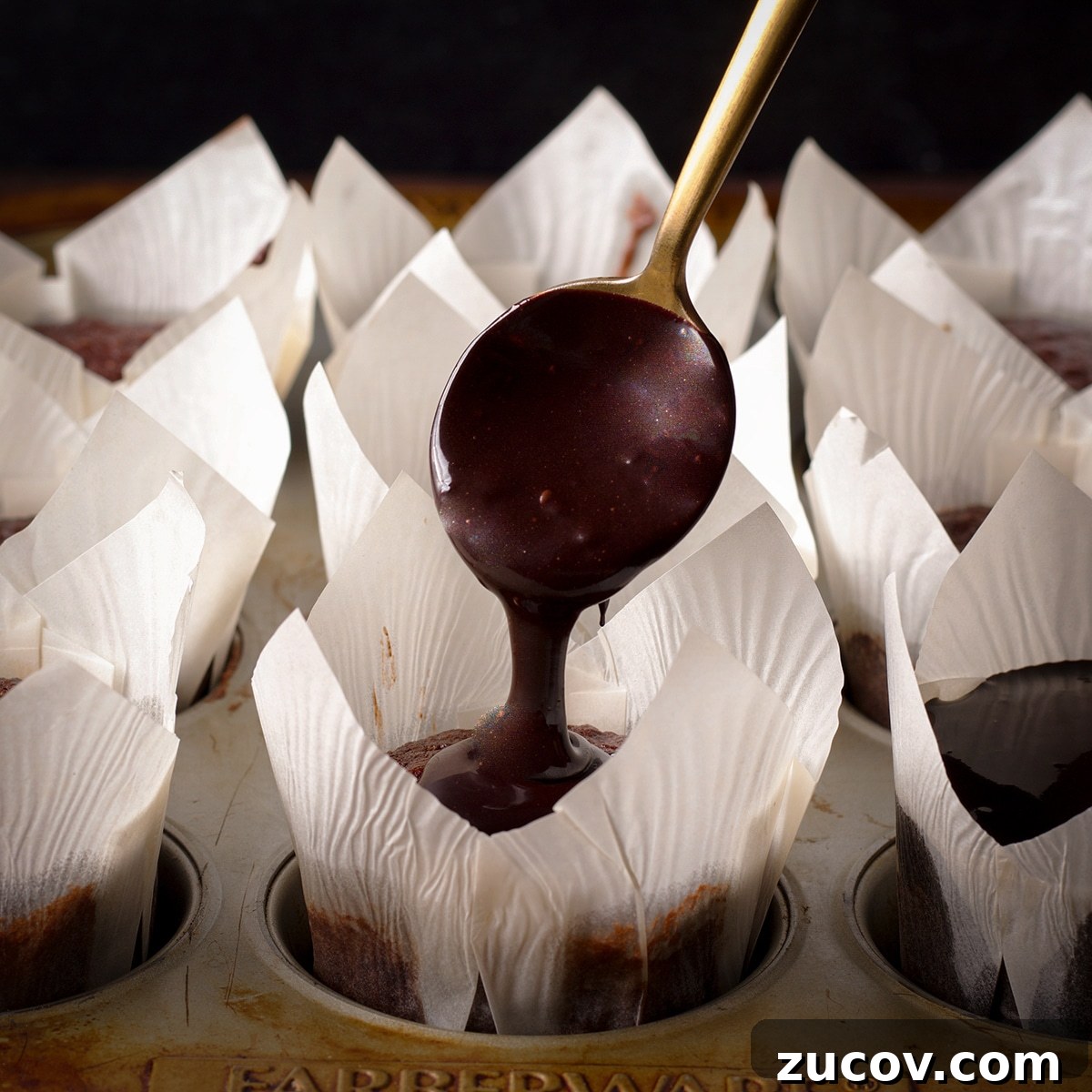 Chocolate Banana Muffins with Oats and Dark Cocoa 12 Someone using a gold spoon to drizzle chocolate glaze over the tops of chocolate banana breakfast muffins.