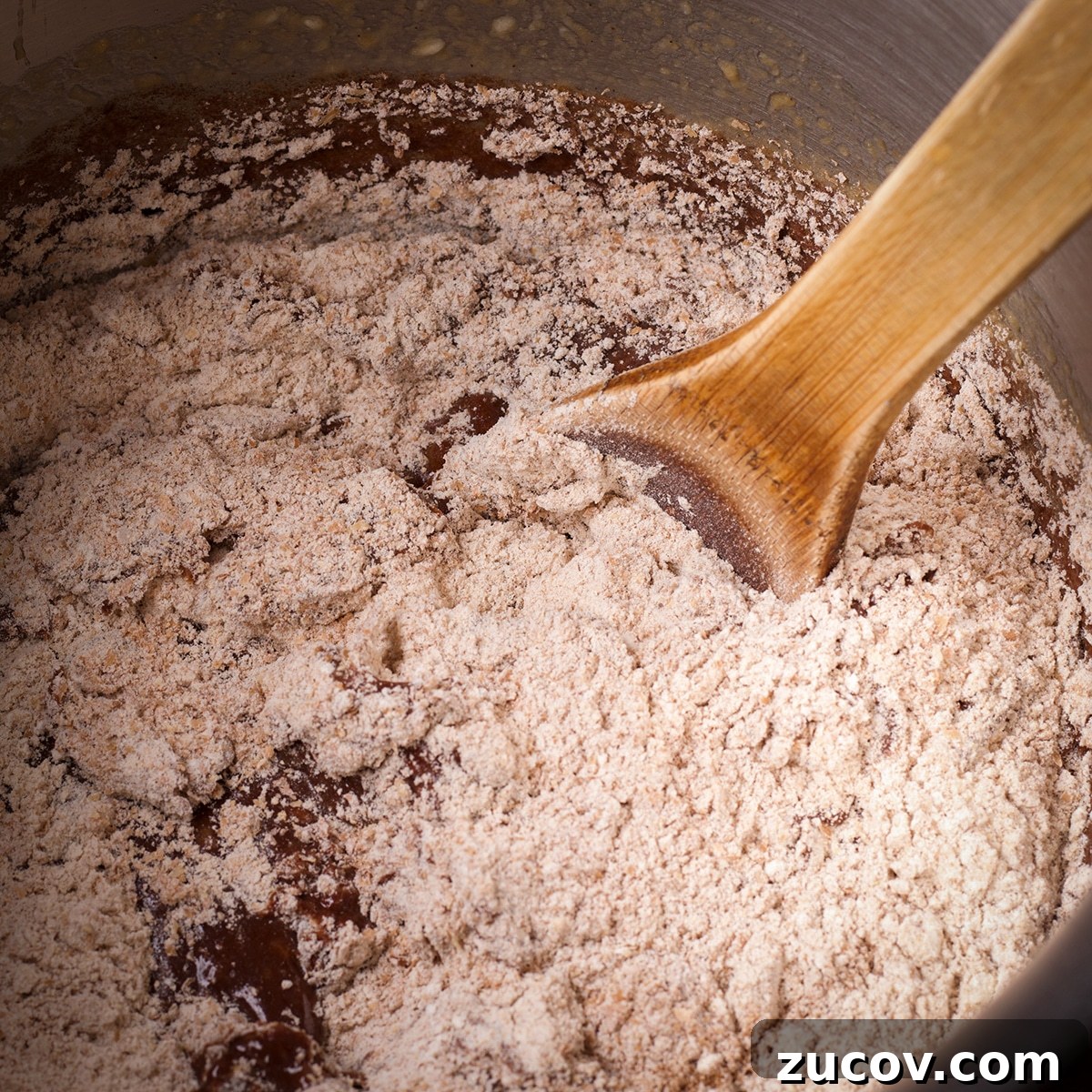 Chocolate Banana Muffins with Oats and Dark Cocoa 9 Someone using a wooden spoon to stir the dry ingredients into chocolate banana muffin batter.